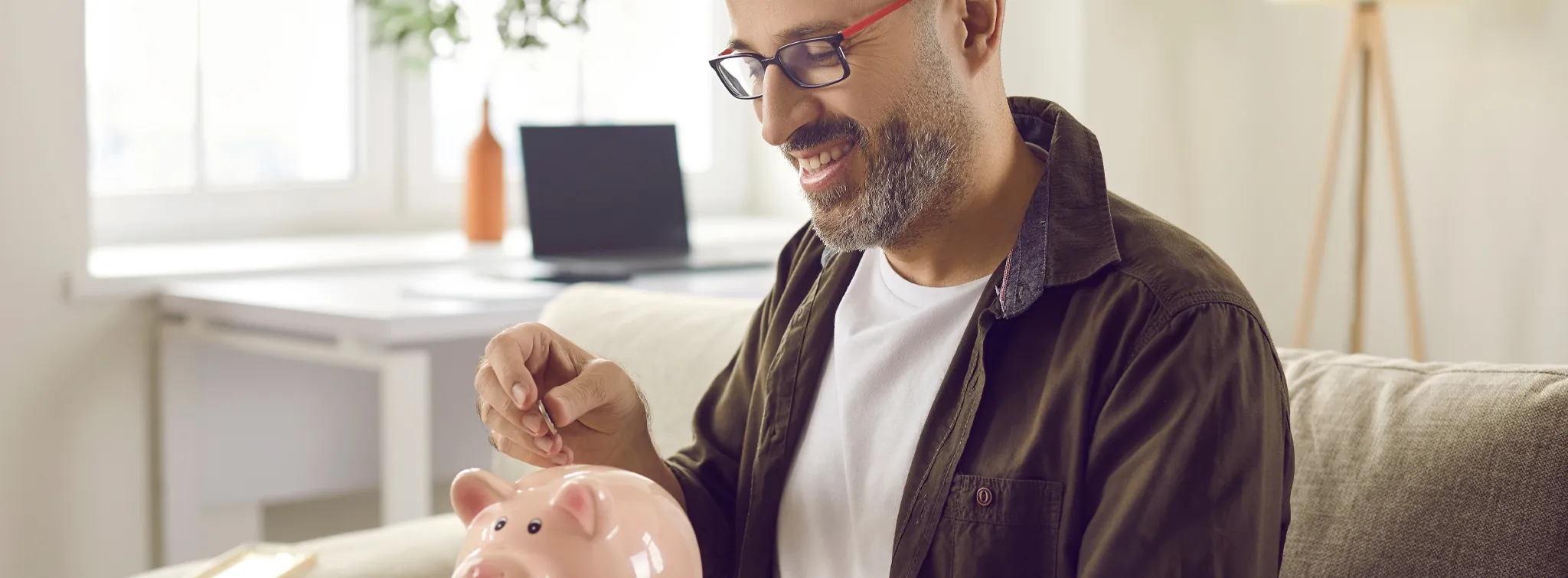 man sitting on a couch putting a coin into a piggybank